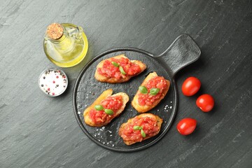 Tasty bruschettas with tomatoes and basil served on black table, flat lay