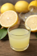 Lemon juice in glass, leaves and fresh lemons on wooden table, closeup