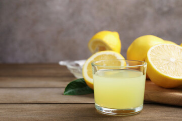 Lemon juice in glass, leaves and fresh lemons on wooden table, closeup. Space for text