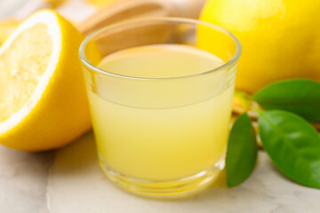 Lemon juice in glass, leaves and fresh lemons on light grey table, closeup