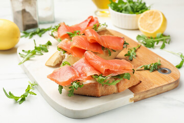 Tasty bruschettas with salmon and arugula served on white table, closeup