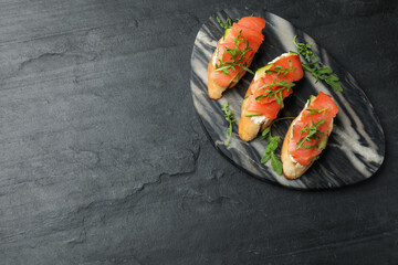 Tasty bruschettas with salmon, cream cheese, cucumber and arugula on black table, top view. Space for text