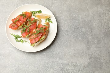 Tasty bruschettas with salmon, cream cheese, cucumber, arugula and lemon on grey table, top view. Space for text