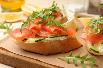 Tasty bruschettas with salmon, cream cheese, cucumber and arugula on table, closeup