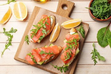 Tasty bruschettas with salmon and cream cheese served on wooden table, flat lay