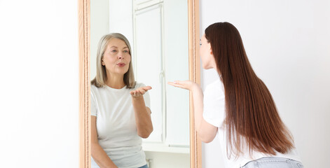 Young girl seeing herself as senior woman in mirror. Concept of personality, past and future, flow of time, age