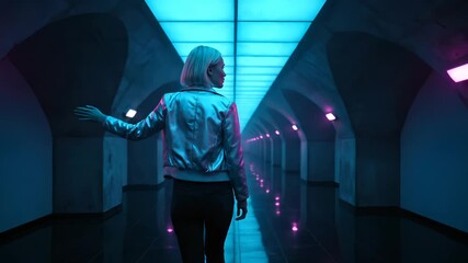 person walk along neon corridor. jacket catch colored light. person move hand near wall while continuing walk. reflection appear on floor. silhouette lead eye into distance. hallway panel glow. - Powered by Adobe