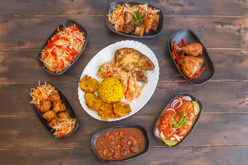 Variété de plats antillais et créoles (accras de morue, colombo de poulet, fricassée de chatrou, court-bouillon de poisson, griot de porc, pikliz, riz Djon Djon, bananes pesées) sur une table en bois 