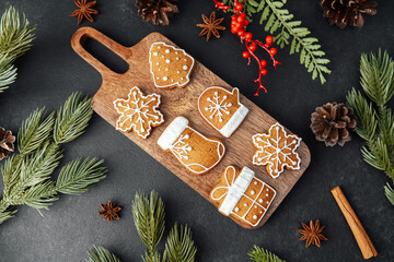 Christmas cookies decorated with icing arranged on a wooden board with pine needles and cones.
