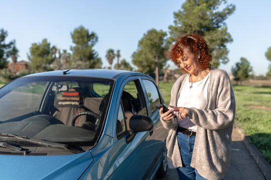 Smiling senior woman standing and using mobile phone app next to her car