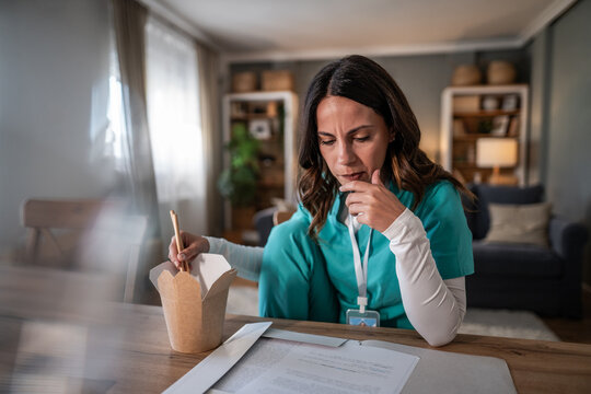 Female nurse working from home eating takeout food and studying