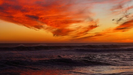 Aerial view of a fiery sunset painting the sky with vibrant oranges and reds over the dark, undulating waves of the ocean, Cape Town, Western Cape, South Africa.