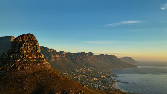 Aerial view of the golden light kissing the rugged peaks of Table Mountain and Lion's Head, casting long shadows over the city and coastline, Cape Town, Western Cape, South Africa.