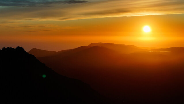 Aerial view of the sun blazing intensely over the shadowy silhouettes of mountains, as if the world is on fire, Cape Town, Western Cape, South Africa.