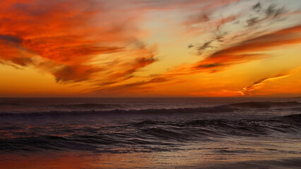 Aerial view of a fiery sunset paints the sky with intense oranges and reds, contrasting with the dark, moody blues of the ocean waves, Cape Town, Western Cape, South Africa.
