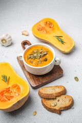 Pumpkin soup in a bowl with roasted bread and butternut squash on a table