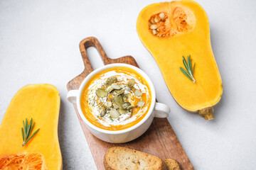 Butternut squash soup topped with seeds served with toasted bread and rosemary on a cutting board