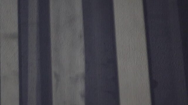 Una toma de cerca de una persiana en movimiento de una ventana reflejada en la pared de una habitaci&oacute;n  con una luz artificial en la noche