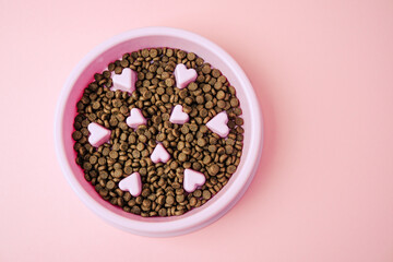 Pink bowl with dog food and heart shapes on a pale pink background
