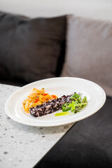 Gourmet black rice dish with creamy sauce and fresh microgreens on white plate.