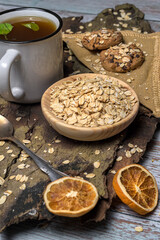 Rustic and healthy breakfast flat laybowl of raw oats, green tea, and oatmeal chocolate chip cookies on a wood and fabric background. Perfect for cozy, natural, and plant based concepts