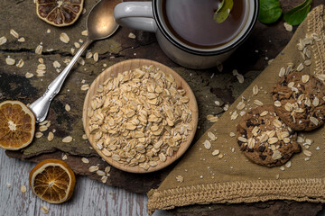 Rustic and healthy breakfast flat laybowl of raw oats, green tea, and oatmeal chocolate chip cookies on a wood and fabric background. Perfect for cozy, natural, and plant based concepts