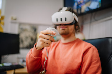 Renceni, Latvia - November 10, 2025: Young man wearing virtual reality headset, holding controller, engaged in immersive gaming experience at home