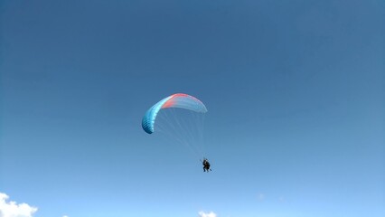 Paraglider flying in clear blue sky, freedom and adventure concept. Minimalist composition with copy space for text or design.
