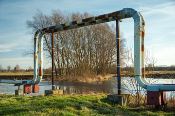 Rusting district heating pipes arched over a flooded field entrance