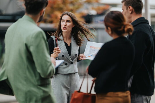 A confident woman leads an outdoor business meeting with colleagues, sharing papers, charts, and strategic notes as autumn colors glow in the background.