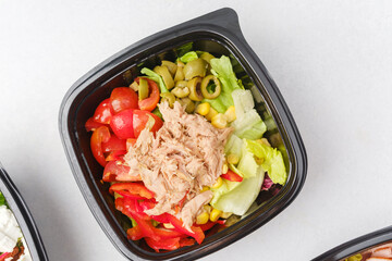 Mixed salads with fresh vegetables meat cheese and greens in black containers for restaurant delivery or meal prep concept