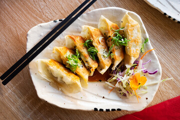 Gyoza dumplings decorated with chopped green onions, Japanese dish on white plate.