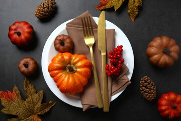 A festive fall table setting with a plate, napkin, cutlery, and pumpkins. Cozy seasonal decor for...