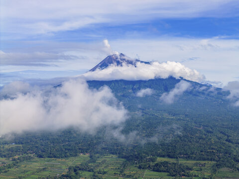 Aerial view of Mount Merapi shrouded in ethereal clouds, its peak kissed by the heavens, a majestic sentinel of nature's raw power, Klaten Regency, Central Java, Indonesia.