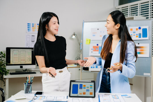 Two UX UI designers collaborating on mobile app wireframes and layouts in modern office. Concept of creativity, teamwork, and digital product design.