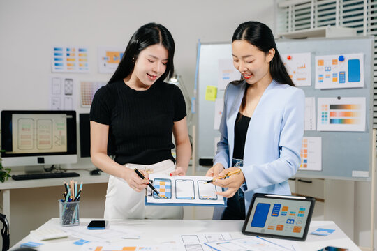 Two UX UI designers collaborating on mobile app wireframes and layouts in modern office. Concept of creativity, teamwork, and digital product design.