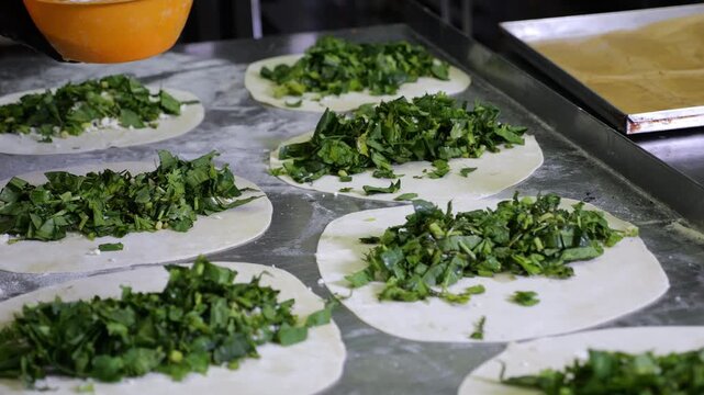Close-up of a chef wearing gloves preparing tortillas with parsley, coriander, dill and spinach in the restaurant kitchen. Traditional flatbreads with herbs, kutabs, gozleme.