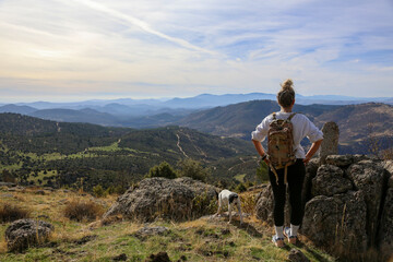 Blonde woman with a bun looking at the mountains after walking along the paths accompanied by her dog