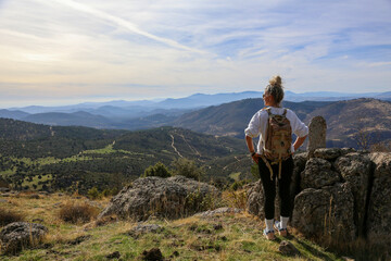 Blonde woman with a bun looking at the mountains after walking along the paths accompanied by her dog