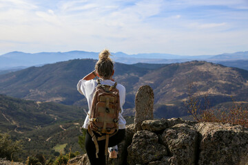 Blonde woman with a bun looking at the mountains after walking along the paths accompanied by her dog
