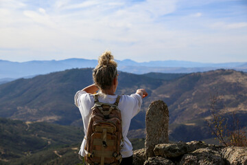 Blonde woman with a bun looking at the mountains after walking along the paths accompanied by her dog