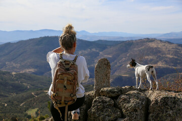 Blonde woman with a bun looking at the mountains after walking along the paths accompanied by her dog