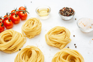 Raw tagliatelle pasta nests with tomatoes and spices on white background