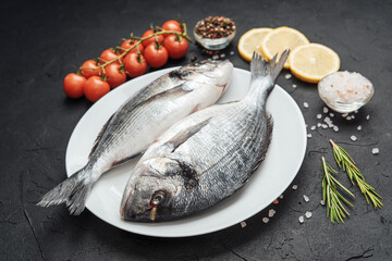 Fresh raw dorado fish on white plate with lemon tomatoes and spices