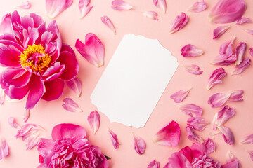 White blank card surrounded by pink peonies and scattered petals on soft pastel background