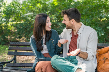 Young couple cuddling on a park bench, smiling and leaning in for a kiss, sharing an affectionate...