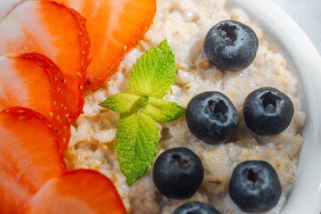 Close up of oatmeal bowl with strawberries blueberries and mint