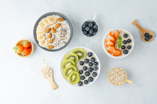 Flat lay of oatmeal bowls with fruits and oats on white background