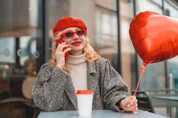 Woman in red hat talks on phone while enjoying coffee and heart balloon
