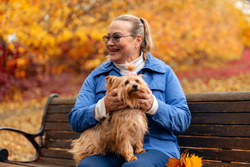 Smiling woman enjoys time with small dog in colorful autumn park